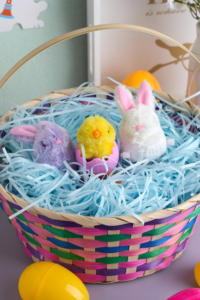 Colorful Easter basket for kids filled with blue Easter "grass" & small stuffed toy bunnies and chicks.