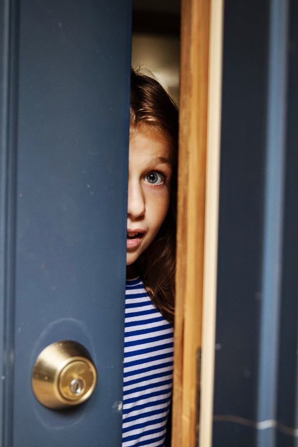 Girl peeking through barely cracked door highlighting the need to teach stranger danger rules.