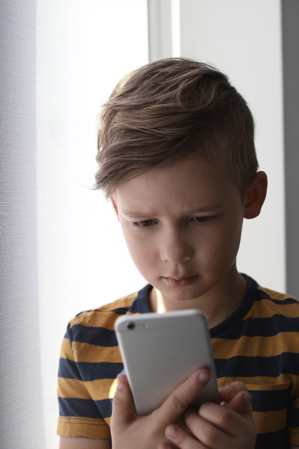 Boy with short hair looking intently at cell. phone, illustrating the possible danger of internet use for children.