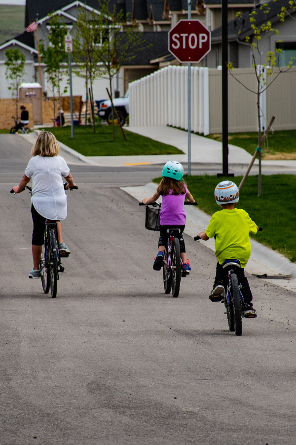 Mother, daughter, and son riding their bikes down the street while wearing helmets, highlighting the importance of proper safety equipment.