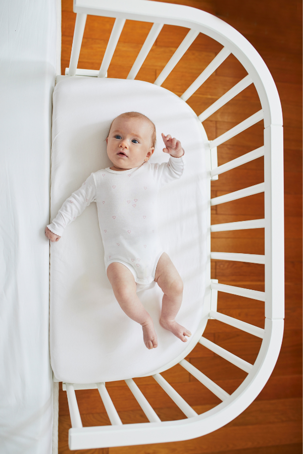 Baby lying on back in crib without unsafe blankets addressing the need to practice safe sleep for babies.