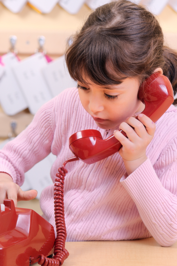 Young girl using a red telephone, emphasizing the importance of establishing clear rules for children when staying home alone.